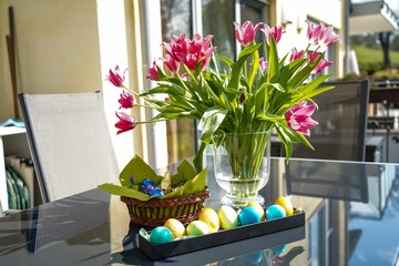 Colored eggs and pink tulips in vase on a sunny day