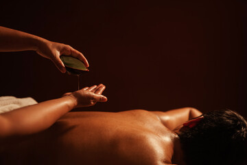 Masseur pouring aroma oil on hand, for massage on back of customer.