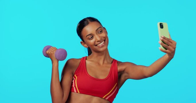 Fitness, woman and dumbbell in studio for selfie, profile picture or workout vlog against a blue background. Happy, fit and sporty female smiling for photo, weightlifting or online post on mockup