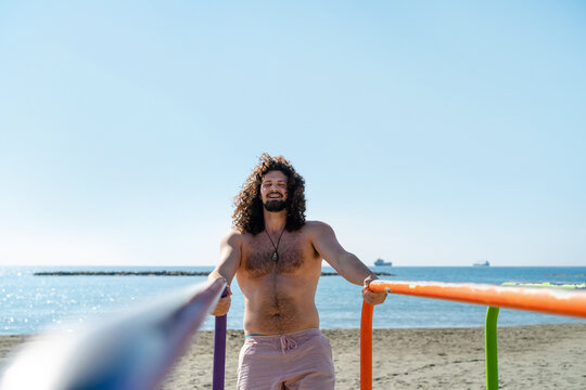 Happy curly shirtless man exercising on the beach