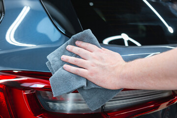 Service worker polishing car with microfiber cloth. Detailing a car - a man holds a soft microfiber in his hand and polishes the body. Selective focus.The concept of proper car washing and car care.