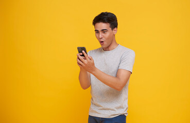Surprised young asian man using mobile phone with positive expression isolated on yellow...