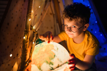 A little boy is pointing a finger at a globe.