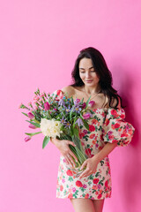Young happy woman stands and holds vase with flowers bouquet in her hands against pink background.