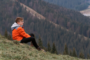 Teenage boy sits on hillside and looking at the distance, thinks about something. Weekend. Travelling with children