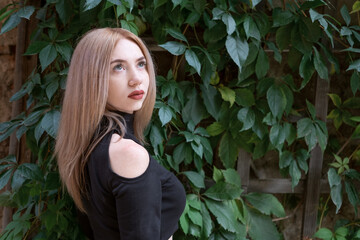 Portrait of young attractive blonde woman in black blouse looks up on green plants background.