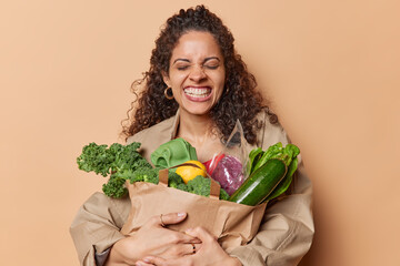 Indoor shot of curly haired brazilian woman smiles broadly shows white perfect teeth embraces paper...