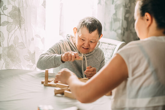 elderly woman with down syndrome and an Asian woman play in tower from wooden blocks