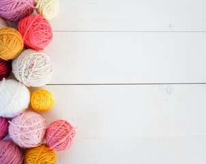 multicolored woolen balls on white wooden ground with space for text, pink, yellow, white