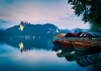 Three lake tour boats standing on famous bled lake with castle on the background and island church. Peaceful relaxing holiday destination in Slovenia.Triglav national park