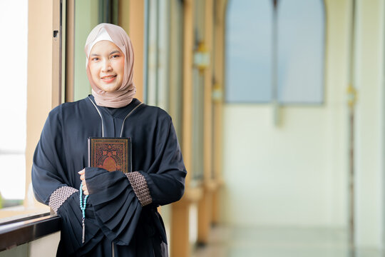 The image of an Asian Muslim woman in the Islamic religion in hijab in cream color. reading the Quran and having a happy smiling face Staying in a beautiful mosque out of respect for God.