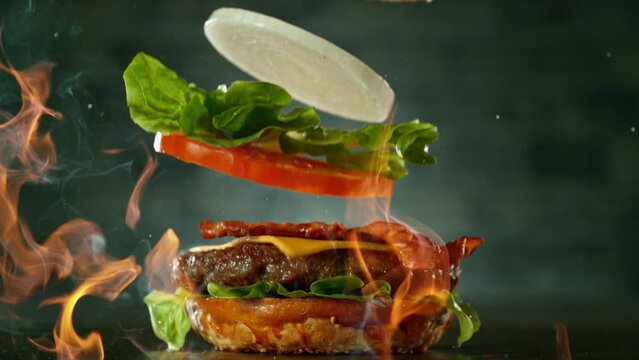 Beef Burger Ingredients Falling and Landing in the Bun with Fire Flames. Camera Move. Super Slow Motion at 1000 fps.