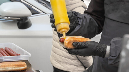 Chef pours mustard sauce over a hot dog before serving it to a customer in a street cafe. Close-up