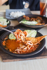 Sambal gami cumi or squid with sambal cooked in earthenware plate against wooden background. Served on wooden table