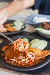 Sambal gami cumi or squid with sambal cooked in earthenware plate against wooden background. Served on wooden table