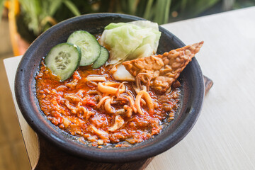 Sambal gami cumi or squid with sambal cooked in earthenware plate against wooden background. Served on wooden table