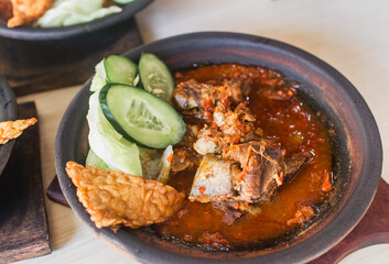 Sambal iga or ribs with sambal cooked in earthenware plate against wooden background. Served on wooden table