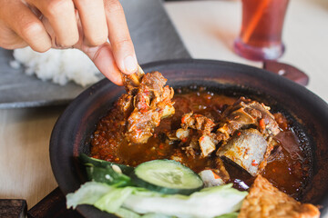 Sambal iga or ribs with sambal cooked in earthenware plate against wooden background. Served on wooden table