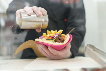 Cook seasoning gyros sandwich with pepper from the shaker. Kitchen worker preparing traditional Greek pita souvlaki in a restaurant