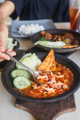 Sambal gami cumi or squid with sambal cooked in earthenware plate against wooden background. Served on wooden table