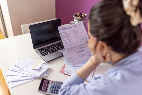 Warried  woman looking at  bills and calculating her monthly expenses and debts. Bankrupt Female having problem income, budget, payment. Paying bills online on laptop at home. Economic crisis