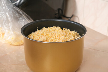 A man puts frozen cheese from freezer grated on grater into bowl of slow cooker. Fast cooking. Cooking lunch dinner for amily at home. process cooking meat in French with potatoes, tomatoes, cheese.