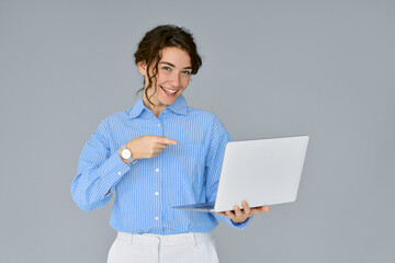 Young happy business woman executive pointing at laptop presenting web service, holding computer advertising software, website or webinar standing isolated on grey background, studio shot.