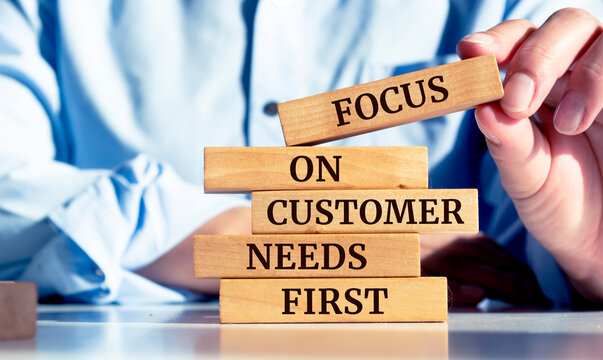 Close up on businessman holding a wooden block with "Focus on customer needs first" message
