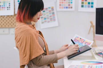 Young graphic designer using a tablet and stylus pen while sitting at her desk in office.