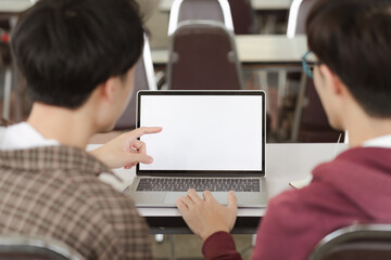A close-up view of two young male university students watching a white screen laptop for graphic...