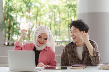 A successful Muslim girl university student and her friends are seen raising their hands in celebration after checking their exam test scores on a laptop at the campus.