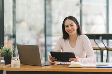 Obraz na płótnie Canvas A portrait of a smiling, young, beautiful, professional, and confident millennial Asian businesswoman using a digital tablet to analyze sales data at a co-working space.