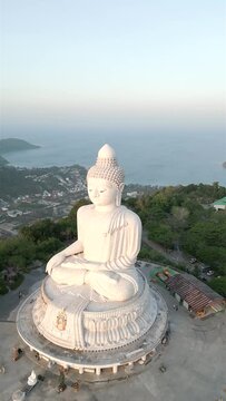 A breathtaking aerial view of the famous Big Buddha statue on the hilltop of Phuket at sunrise, with the stunning ocean and coastline surrounding the island in the background.