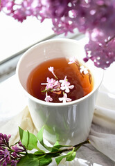 The postcard is beautiful. A mug of tea, an old book and a bouquet of purple lilac. A beautiful still life. Spring time. The concept of Good morning.