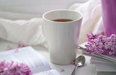 The postcard is beautiful. A mug of tea, an old book and a bouquet of purple lilac. A beautiful still life. Spring time. The concept of Good morning.