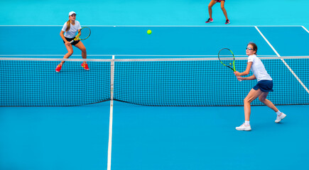 Tennis players play mixed doubles on blue hard courts on a bright sunny day