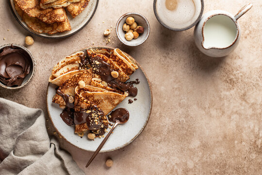 Crepes with chocolate and hazelnuts on beige background. Thin pancakes as delisious breakfast or dessert concept, Pancake day, Maslenitsa. Top view, copy space