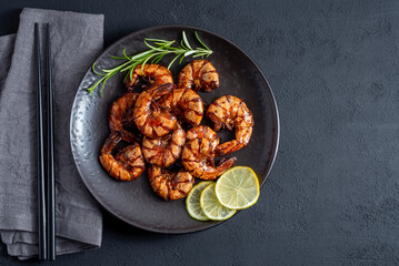 Grilled fried shrimp on a black plate dark background top view