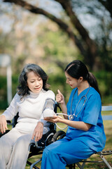 Fototapeta na wymiar Elderly asian senior woman on wheelchair with Asian careful caregiver. Nursing home hospital garden