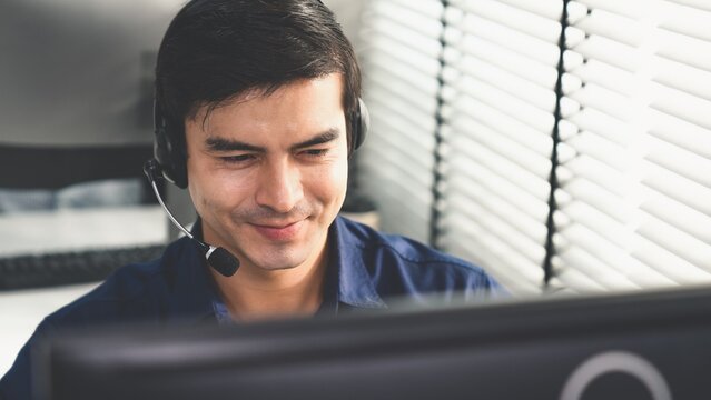Young competent asian male call center agent working at his computer while simultaneously speaking with customers. Concept of an operator, customer service agent working in the office with headset.
