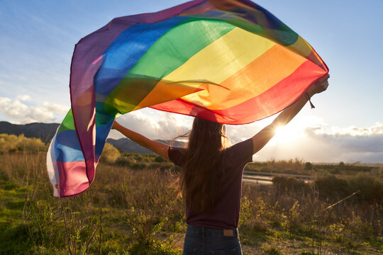 Non-binary person waving LGTB flag in the meadow