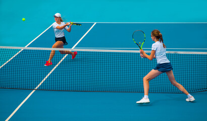 Fototapeta na wymiar A girl plays tennis on a court with a hard blue surface on a summer sunny day 