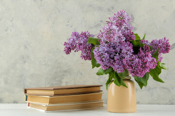Spring bouquet of lilacs in a vase and books on a light background