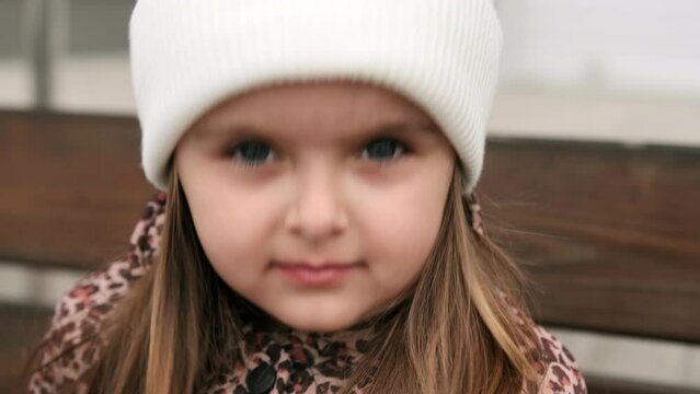 Portrait of a sad little girl in a white hat looking directly into the camera. Close-up.