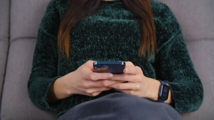 Young woman typing sms message on a cellphone. Unrecognizable female person texting online with a modern smart phone at home