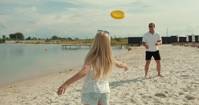 Father and daughter play frisbee on the beach