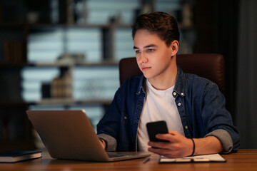Young guy businessman working at office, using laptop and smartphone