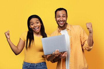 Glad excited millennial african american couple with laptop and open mouth making victory and success gesture