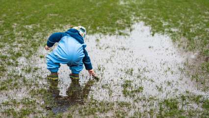 A little child playing in a puddle in a park during rainy weather