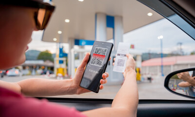 Woman using contactless payment by mobile phone with QR code at car filling station
